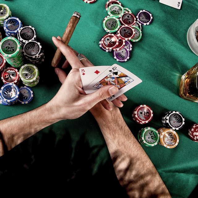7 steg som du kan ta nu för att försöka bekämpa ditt beroende av spel, shopping, mat och annat 2 Ett par händer som håller i spelkort och en cigarr över ett bord med spelmarker och ett glas sprit.