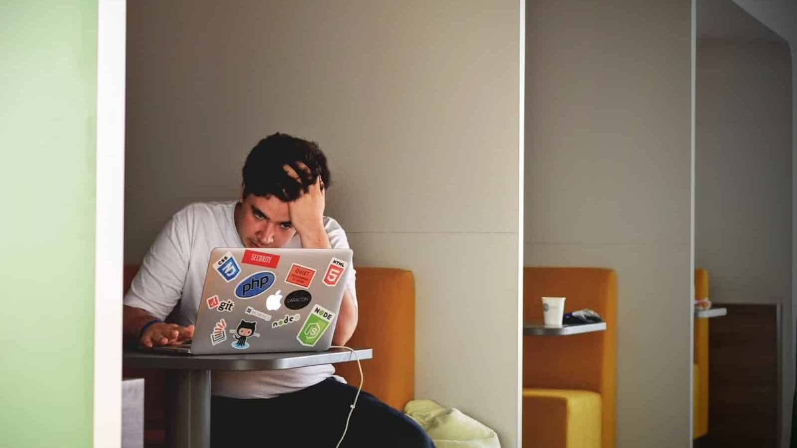 Slå ihop lån och spara pengar! 1 Man i vit tröja använder MacBook för att lära sig mer om att slå ihop lån